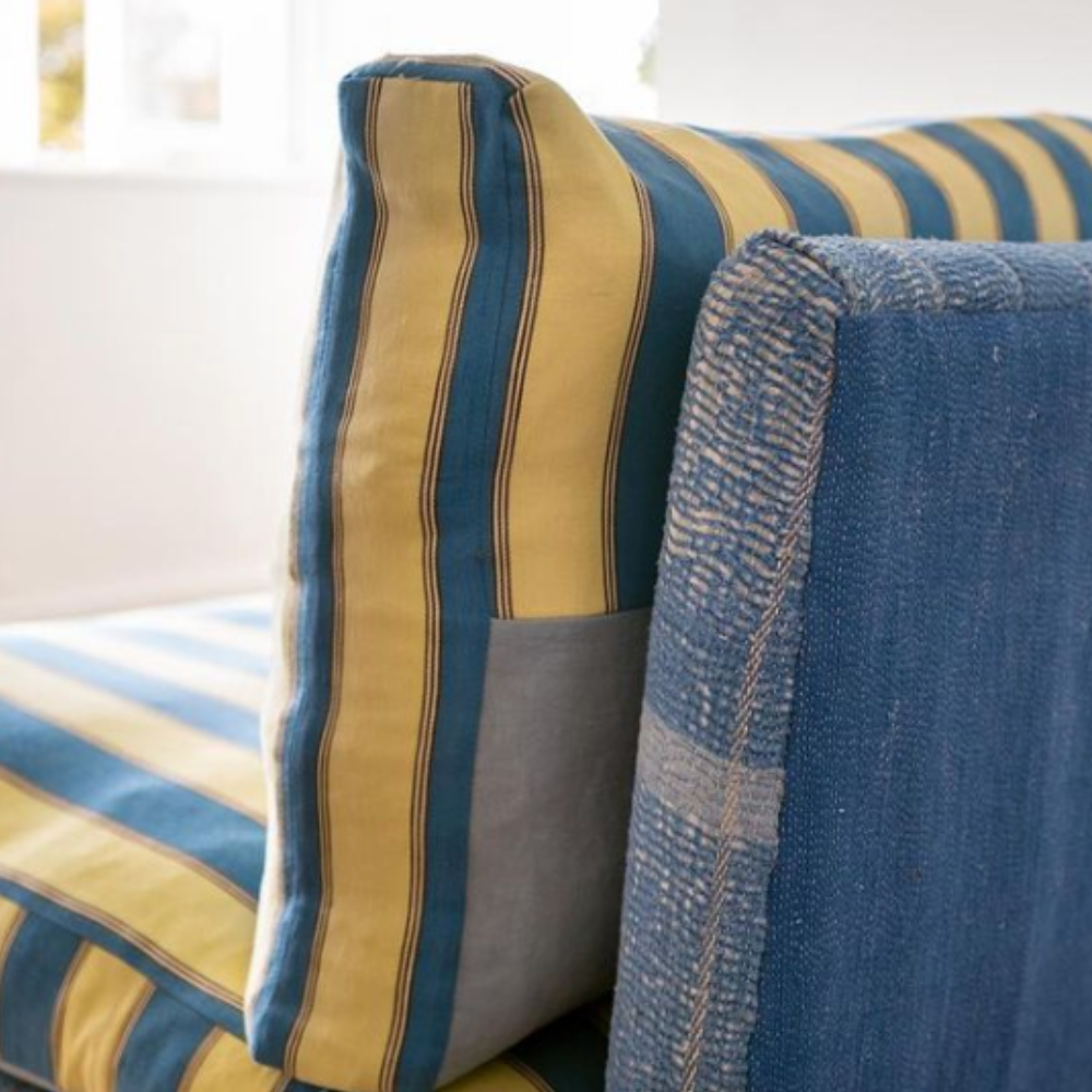 Blue sofa with stripy yellow and blue cushions facing a window.