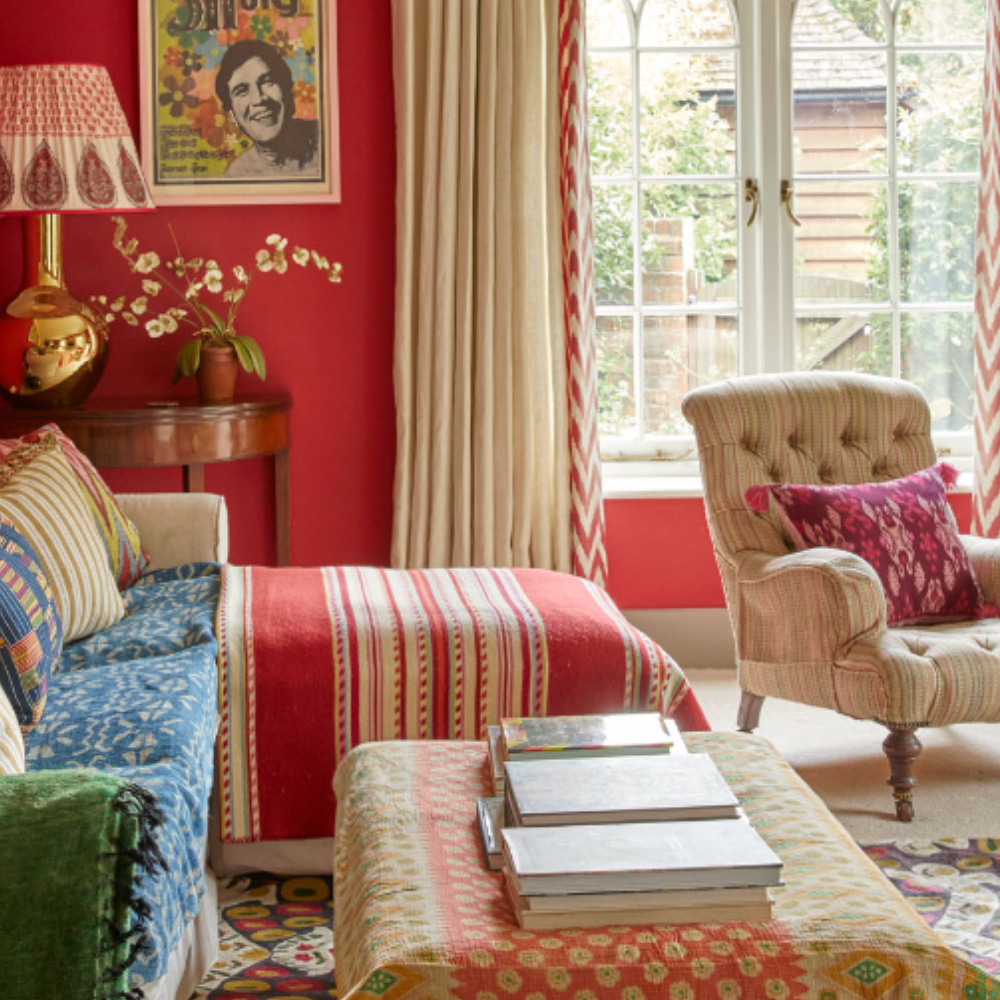 Bright and colourful room with red walls and a green and blue sofa. It has a cosy and comfortable style with bold lamps and a maximalist style.