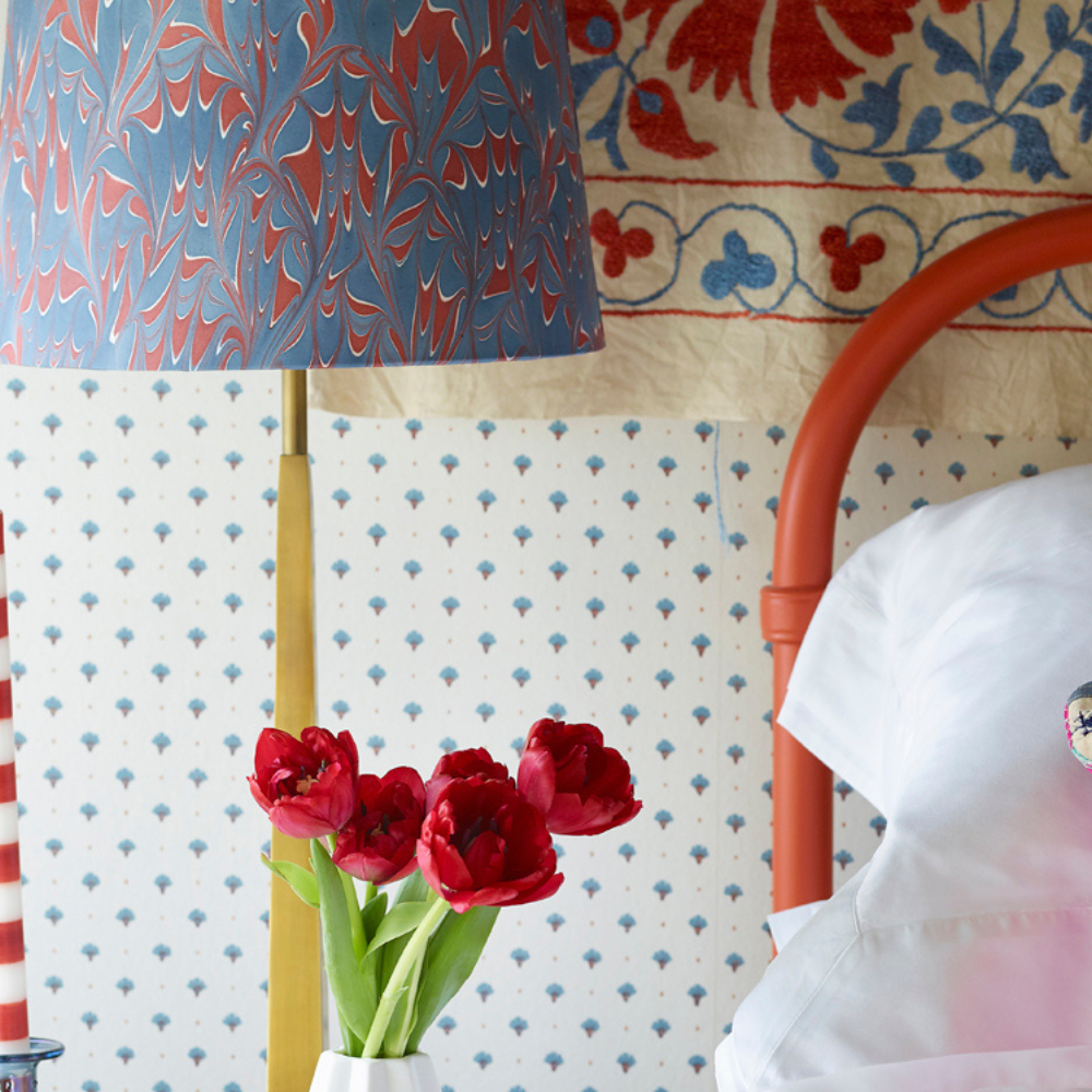 Close up of a red bed frame with brightly coloured cushions and lamp. A red and white striped candle sits on the bedside table.